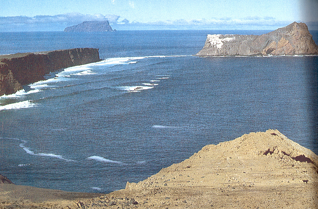 A panoramic view shows the crater ring of San Félix volcano, with Isla San Ambrosio on the horizon.  San Félix Island, 800 km west of the Chilean coast, consists largely of a low lava platform separating two tuff cones.  The Islota Gonzáles cone (right) is separated from the main island by a shallow submerged platform.  Cerro Amarillo at the NW end of the island is the source of fresh-looking lava flows that reached the sea and formed the low lava platform.   Photo by Oscar González-Ferrán (University of Chile).
