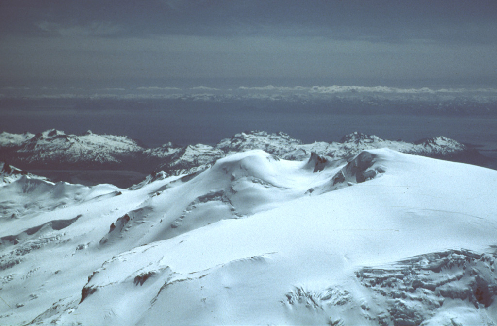 The almost completely ice-covered Kukak is near the NE end of a chain of volcanoes extending from Mount Katmai. Kukak, seen here from the NW with Shelikof Strait in the background, contains a vigorous fumarole field on its northern summit.  Photo by Christina Neal, 1990 (U.S. Geological Survey, Alaska Volcano Observatory).