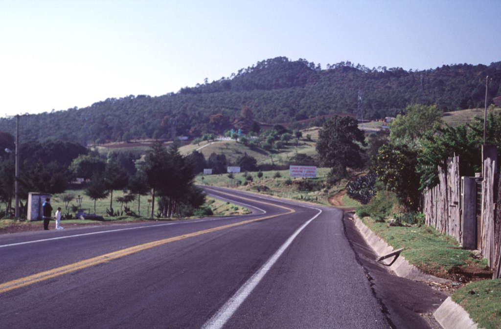 The hill on the  horizon is El Volcanicillo, a scoria cone that produced two lava flows down opposite sides of a ridge on the NE flank of Cofre de Perote volcano. The forested area extending across the photo below the cone is the Río Naolinco lava flow, a massive 900-year-old pahoehoe flow that reached as far as 50 km from El Volcanillo; the ‘a’a Toxtlacuaya flow traveled down the opposite side of the ridge. Highway 140 is in the foreground. Photo by Lee Siebert, 2000 (Smithsonian Institution).