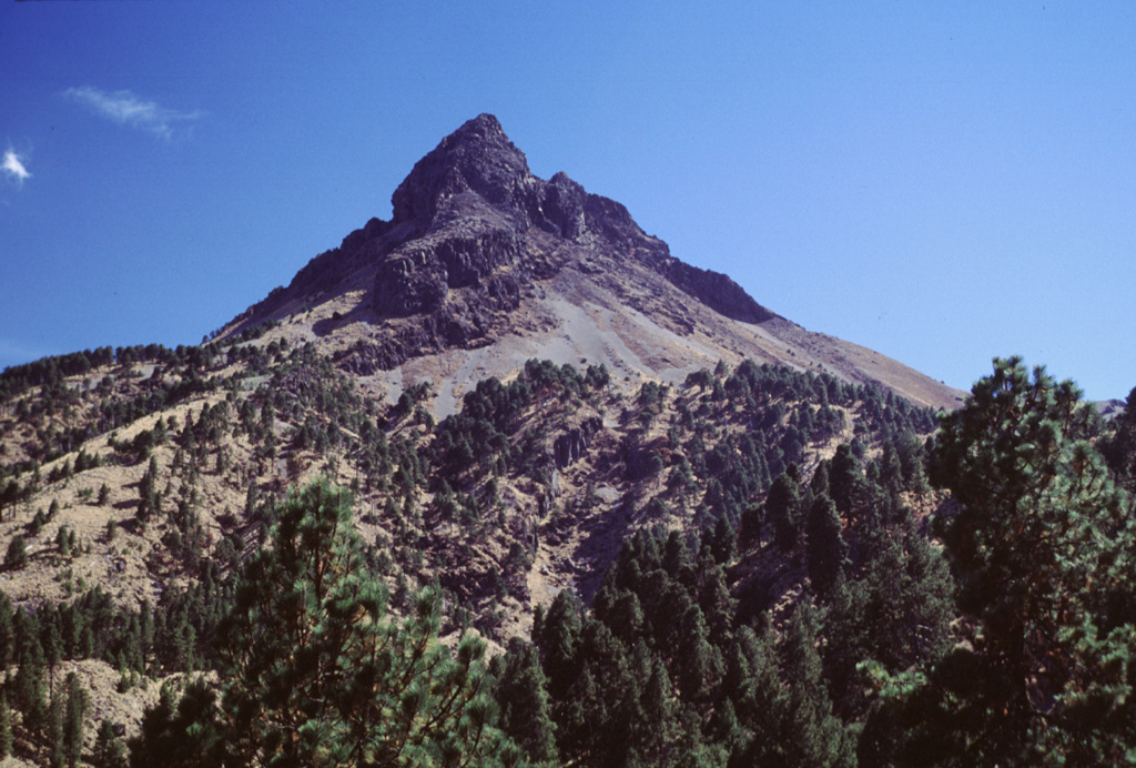 The summit of Nevado de Colima is the highest peak in western México and has been extensively eroded by glaciers, exposing steeply dipping lava flows. This cone is seen here from the northern rim of the outer collapse scarp, which contains a younger scarp on its NW side. This smaller 5-km-wide scarp formed during the late Pleistocene as a result of the collapse of the Nevado II edifice. Photo by Lee Siebert, 2000 (Smithsonian Institution).