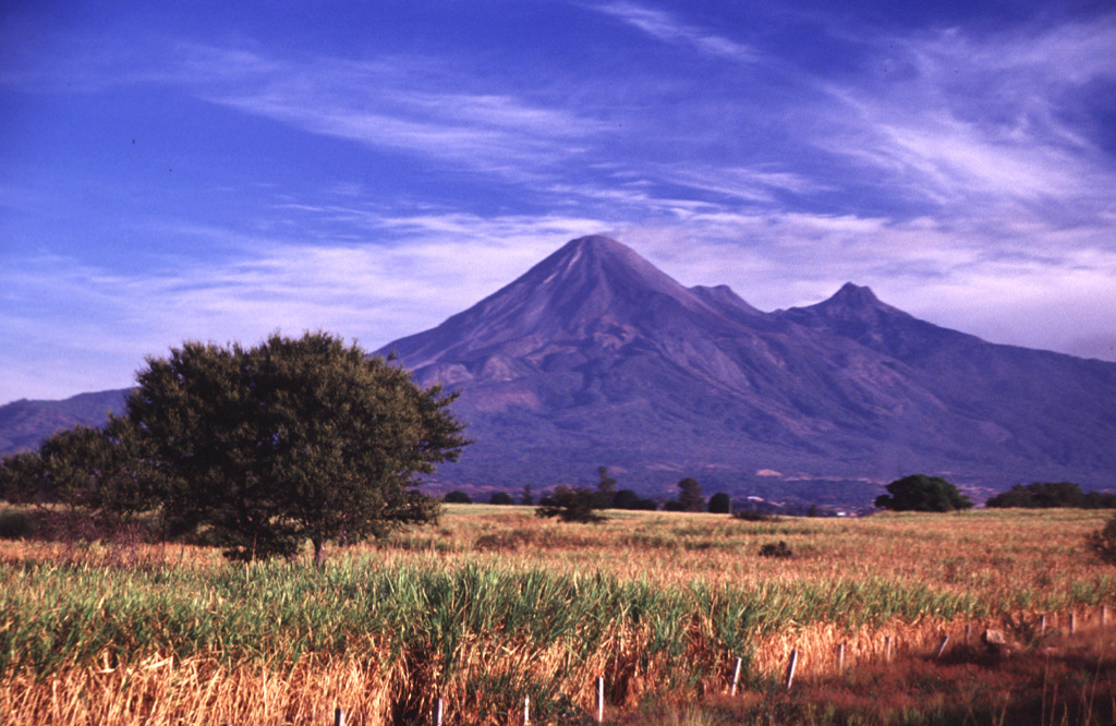 The Colima volcanic complex towers above the floor of the Colima graben. Volcán de Colima is seen here from the SE, with Nevado de Colima, the highest peak in western México, to the right. The flat ridge between the peaks is El Volcancito, a lava dome that began growing in 1869 on the NE flank. The Colima complex, including Volcán Cántaro to the north, forms the westernmost of three major N-S-trending volcanic chains perpendicular to the E-W trending Mexican Volcanic Belt. Photo by Lee Siebert, 2000 (Smithsonian Institution).