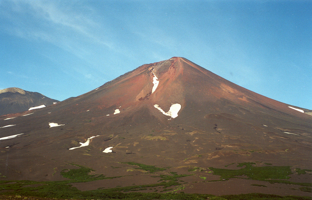 Chikurachki, the highest volcano on Paramushir Island, is a relatively small cone constructed on a Pleistocene edifice. The eastern side is seen here with oxidized (orange-red) scoria covering the upper part of the cone. The peak to the left is part of the Tatarinov group of six volcanic centers, located immediately to the south. The Tatarinov volcanoes are eroded and all but one of the historical (pre-2000) eruptions of the Chikurachki-Tatarinov complex have occurred from Chikurachki. Photo by Alexander Belousov, 2000 (Institute of Volcanology, Kamchatka, Russia).