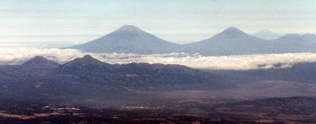 The two small peaks to the left are part of the Telomoyo volcanic complex, which was constructed along a NNW-SSE-trending line of volcanoes extending from Ungaran in the N to Merapi in the S. Telomoyo filled much of the southern side of a depression formed by collapse of the Pleistocene Soropati volcano and grew to a height of 600 m above its rim. The two large peaks in the background are Sumbing (L) and Sundoro (R), with Slamet volcano on the far-right horizon. Photo by Hideko and Minoru Kusakabe, 2000 (Okayama University).