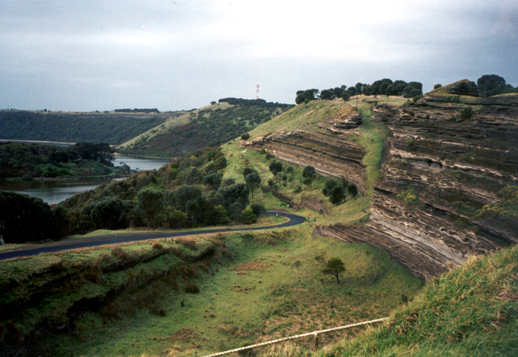 Tower Hill maar, with bedded pyroclastic layers exposed in its wall, is part of the voluminous Newer Volcanics Province, which covers a broad 15,000 km2 area of SE Australia. The volcanic field contains nearly 400 vents, with late-Pleistocene to Holocene eruptions producing scoria cones, maars, tuff rings, and valley-filling lava flows. The most recent eruptions took place at Mount Schank and Mount Gambier. Photo by Monica Handler, 1995 (Carnegie Institution).