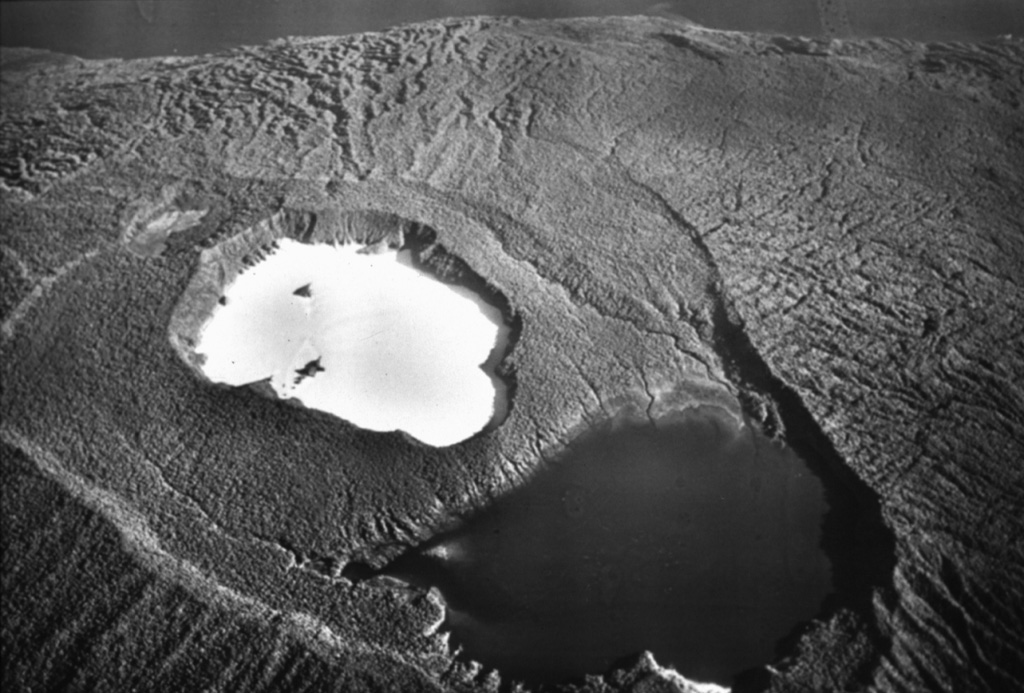 An aerial overflight during World War II shows the summit of Ambae volcano from the SE. A broad cone containing three crater lakes is located at the summit within the youngest of at least two nested calderas. Post-caldera explosive eruptions formed the summit crater of Lake Voui (the light-colored lake) about 360 years ago. Lake Manaro Lakua at the lower right (also known as Manaro Ngoru) is alongside the eastern caldera wall. Photo by U.S. Air Force (courtesy of Claude Robin, ORSTOM; Bull. Global Volcanism Network, 1995).
