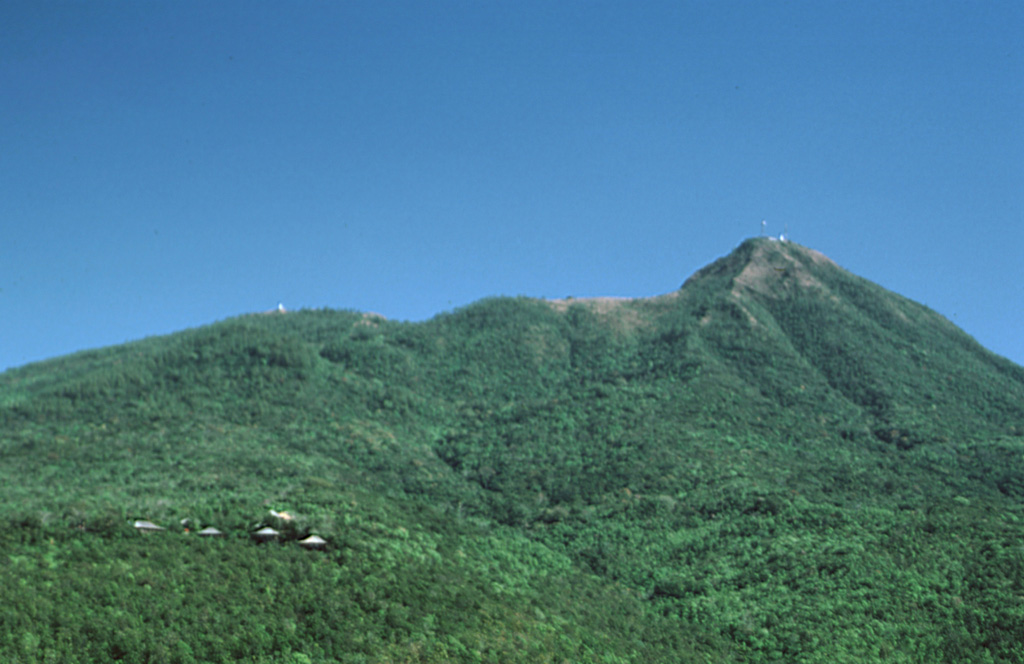 Mount Popa in central Myanmar is seen here from the town of Popa on the W flank. The summit of the volcano forms the back headwall of a large horseshoe-shaped collapse scar produced by collapse of the edifice. This 1.6-km-wide, 850-m-deep crater opens to the NW, in the direction of the ridge on the left horizon. The 3 km3 debris avalanche deposit to the N covers an area of 27 km2. Photo by Sorena Sorensen, 2000 (Smithsonian Institution).