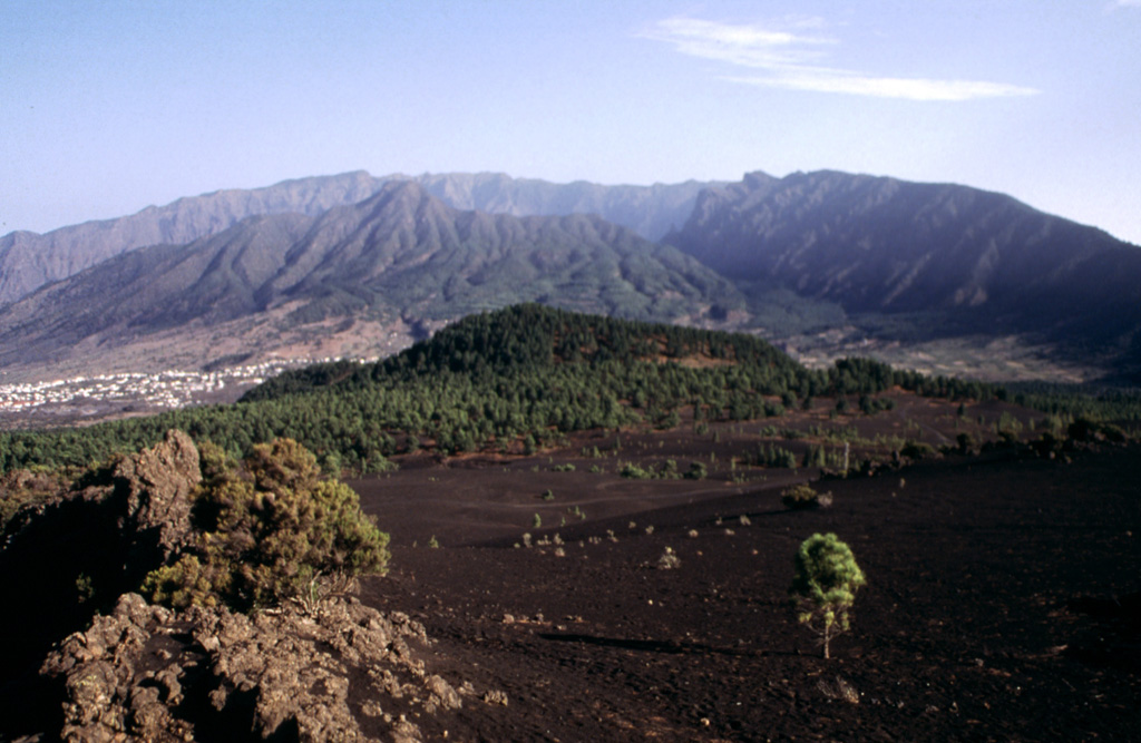 The caldera rim of the Taburiente volcano, which makes up the northern section of the island of La Palma, is seen here from a lava flow field on the southern volcano, Cumbre Vieja. Bejenado volcano (left center) is located on the southern edge of the breached Taburiente caldera. Cumbre Nueva Ridge (right) was formed by a large-scale collapse. Cumbre Vieja is the most recently active volcanic center on the island, with numerous cones and lava flows. Photo by Yasuo Miyabuchi, 1997 (Forestry and Forest Products Research Institute, Kyushu).