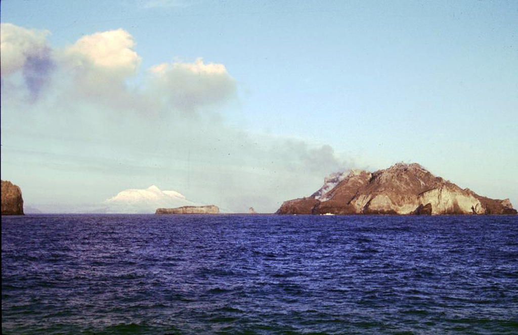 Three small, low islands on the Kerguelen Plateau form the McDonald Islands. The largest island, McDonald, is only 1 km2 in area and around 200 m high. This April 1997 photo shows a plume at Samarang Hill (right). The Island is composed of a layered tuff plateau cut by dikes and lava domes. A possible nearby active submarine center was inferred from pumice that washed up on Heard Island in 1992. The snow-capped peak in the background is Heard volcano, 44 km to the E. Copyrighted photo by Richard Williams, 1997 (Australian Antarctic Div., published in Global Volcanism Network Bulletin).