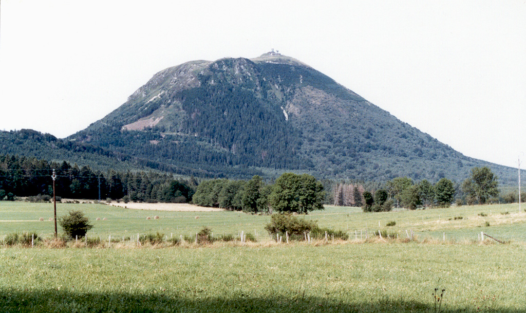 The southern flanks of Puy de Dôme, the highest peak of the Chaîne des Puys volcanic chain, rises above farmlands. Puy de Dôme originated during a series of eruptions about 10,000 years ago. Explosive destruction of the eastern side (right) of a massive lava dome was followed by growth of a second dome. Crumbling of a spine capping the second dome formed the low mound of breccia at the summit of Puy de Dôme, which has been covered by a pyroclastic flow deposit from nearby Killian volcano. Photo by Ichio Moriya (Kanazawa University).