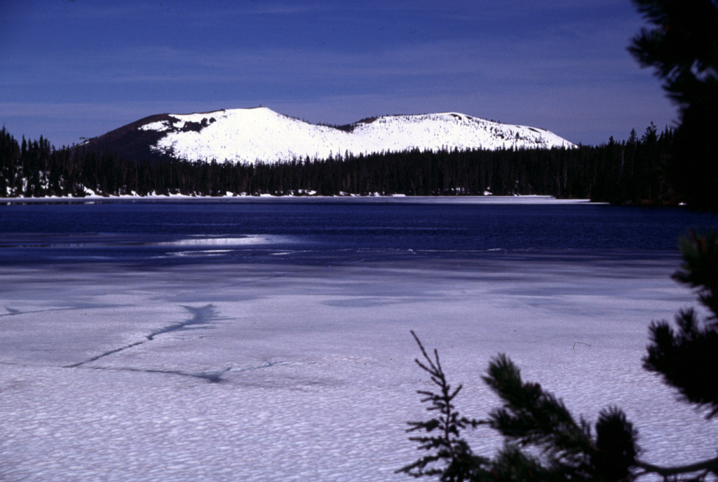 The Sand Mountain scoria cones rise to the WNW in late Spring across the partially frozen surface of Big Lake. South (left) and North Sand Mountain cones are the largest of a group of 23 scoria cones along a N-S line immediately west of the Cascade crest, NW of Mount Washington. A series of young, sparsely vegetated lava flows reaching the McKenzie River valley originated from vents to the west side and erupted primarily during about 3,000-4,000 years ago. Photo by Lee Siebert, 2000 (Smithsonian Institution).