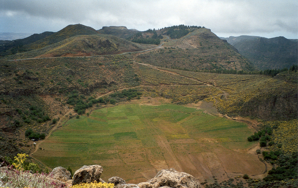 Agricultural field on the floor of Marteles Maar are seen in the foreground, with several cinder cones in the background. These are part of a group of Quaternary monogenetic volcanoes in northern Gran Canaria. Eruptions of Holocene age have been restricted to the northern, primarily north-eastern, part of the island, including at Las Isletas, a peninsula on the NE coast.  Photo by Alexander Belousov, 2001 (Institute of Volcanology, Kamchatka, Russia).