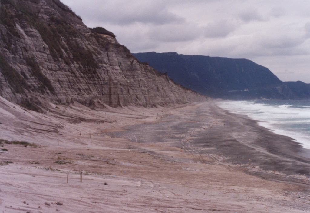 Stratified phreatomagmatic deposits are exposed along a cliff on the eastern coast of Niijima, with the flat-topped Miyazukayama lava dome in the background. The 11-km-long island is comprised of eight rhyolite lava domes clustered in two groups. The Mukaiyama complex at the southern end of the island and Achiyama lava dome at the northern end formed during the 9th century CE. Photo by Ichio Moriya (Kanazawa University).