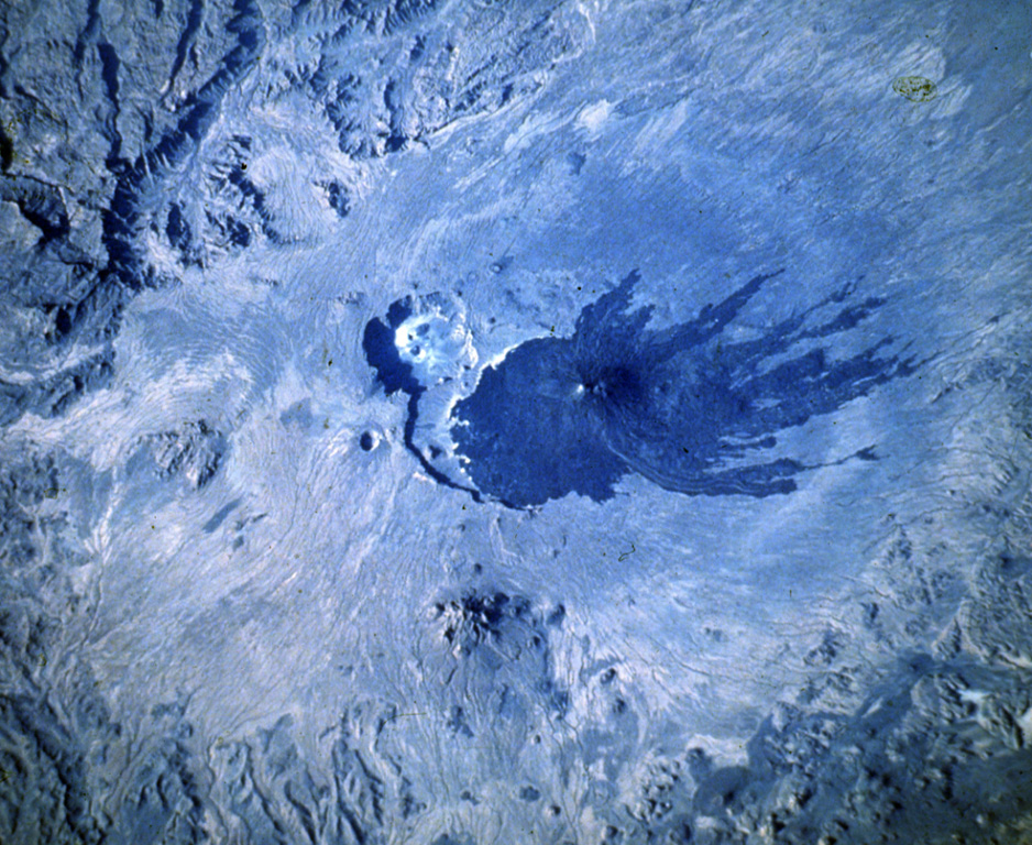 Dark lava flows radiate from Toussidé volcano (center), the second highest peak of the Tibesti Range in Chad. N to the bottom of this Space Shuttle image. It was constructed at the W end of the large Pleistocene caldera of Yirrigue, whose scarp is seen left of Toussidé. The smaller 8-km-wide caldera of Trou au Natron cuts the SE rim of the caldera. Ehi Timi (lower center) and Ehi Sosso (left center) volcanoes are located on the flanks of the massif. NASA Space Shuttle image S-511-42, 1985 (http://eol.jsc.nasa.gov/).