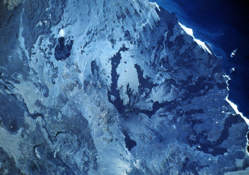 Dark-colored lava flows radiate away from the summit of Dubbi volcano in this Space Shuttle image with the Red Sea at the upper right. The two most recent eruptions were fed by fissure systems that extend NW-SE and NNE-SSW. The former produced lava flows that reached the Red Sea in 1400 CE. Lava flows from the 1861 eruption traveled as far as 22 km to the east and also reached the coast. Photo S-61A-36, 1985 (National Aeronautical and Space Administration).