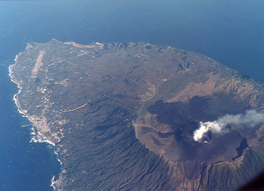 A plume rises from the crater of Miharayama on Oshima island. It lies within a 4-km-wide caldera, the rim of which is prominently visible in this aerial photo from the SW. Dark-colored lava flows from the 1986 eruption cover part of the caldera floor. More than 40 cones are located within the caldera and along two parallel rift zones trending NNW-SSE across the island. The port city of Motomachi on the west coast is to the left and the island's airport is at the upper left. Photo by Ichio Moriya (Kanazawa University).