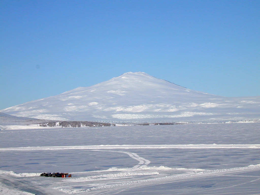 Mount Melbourne towers above the ice shelf of the Ross Sea in Antarctica's Northern Victoria Land. The glaciated edifice contains a large number of scoria cones, lava domes, and viscous lava flows. Lava fields are exposed at the summit and upper flanks. Fumarolic activity has been observed and there are corresponding tephra layers within and on top of surrounding ice layers. Photo by Arrigo Caserta, 2000 (Istituto Nazionale di Geofisica e Vulcanologia, Roma).