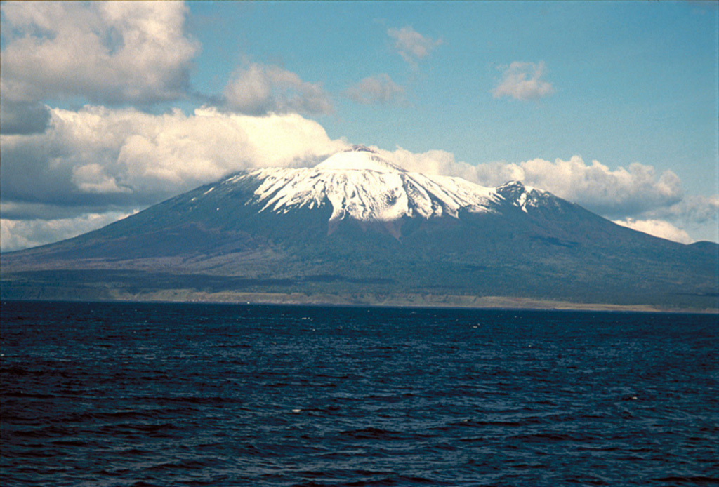 The SE flanks of Chachadake volcano in the Kuril Islands rise above the Pacific Ocean at the NE tip of Kunashir Island. A cone has formed in the 2.1 x 2.4 km summit caldera and is seen here rising above the center of the edifice. A major explosive eruption in 1973 and a smaller eruption occurred in 1812. Copyrighted photo by Yoshihiro Ishizuka, 1992 (Japanese Quaternary Volcanoes database, RIODB, http://riodb02.ibase.aist.go.jp/strata/VOL_JP/EN/index.htm and Geol Surv Japan, AIST, http://www.gsj.jp/).