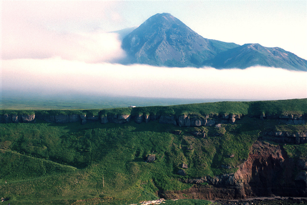 Nemo Peak, seen here from the south, is the northernmost of two large volcanoes forming Onekotan Island. The cone initially formed in four stages beginning in the early Holocene. Construction of the cone within the youngest of three large calderas has left a crescent-shaped lake at the NE end of this 5-km-wide caldera. The final activity built a lava dome in the 350-m-wide summit crater.  Photo by Yoshihiro Ishizuka, 2000 (Hokkaido University).