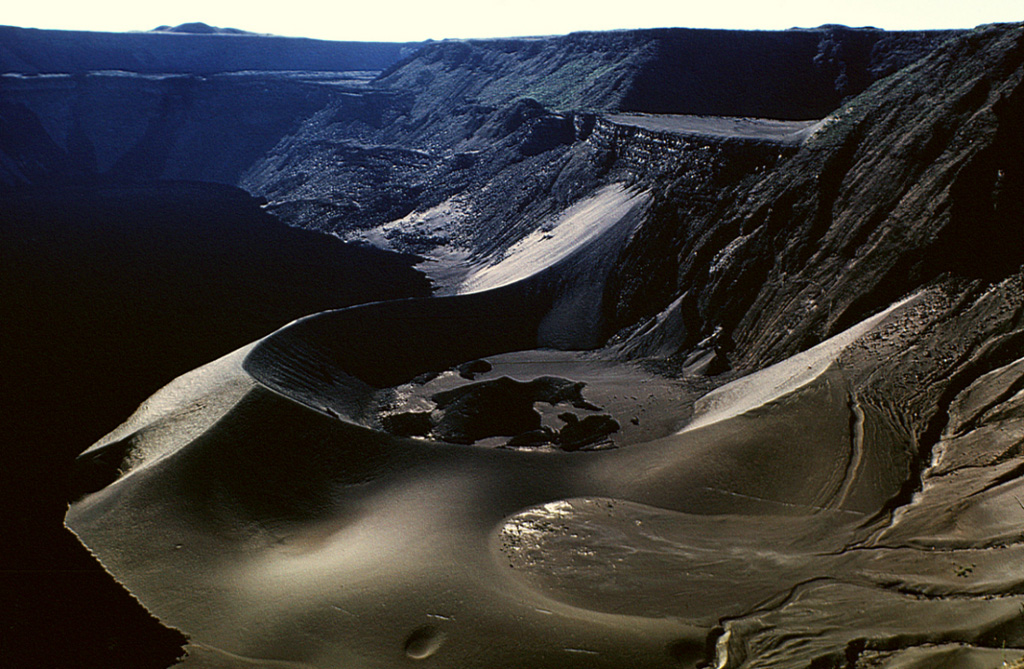 A large tuff cone occupies the ENE side of the summit caldera of Cerro Azul volcano at the SW tip of Isabela Island.  A small caldera bench is seen above the cone at the upper right, and a larger bench on the northern side of the caldera is outlined by the light-colored line below the horizon at the upper left.  The 4 x 5 km wide caldera is one of the smallest of the Galápagos shield volcanoes, but its 650 m depth makes it one of the deepest.  Youthful dark-colored lava flows at the left cover much of the caldera floor. Photo by Tom Simkin (Smithsonian Institution).