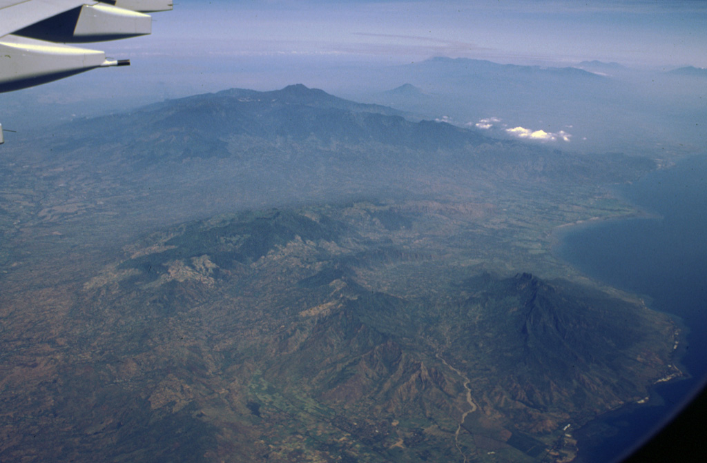 The broad volcanic complex in the center of this aerial view from the NE is the Iyang-Argapura massif, which lies west of Raung volcano (out of view to the left). The smaller conical volcano beyond and to the right of the summit of Iyang-Argapura is Lamongan volcano, and the elongated Tengger-Semeru range lies at the right of the horizon. The Pleistocene Ringgit volcano lies along the coast at the lower right. Photo by Lee Siebert, 2000 (Smithsonian Institution)