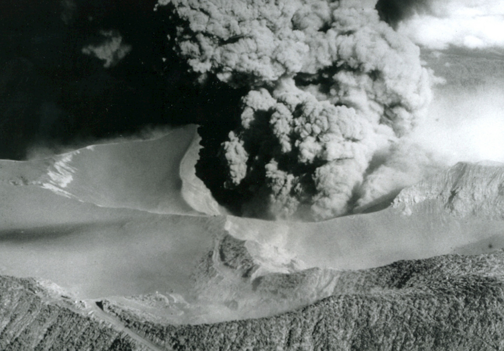 An ash plume erupts from the Irazú summit crater on 14 April 1964, about midway through a major explosive eruption that began in 1963. The ash-covered plateau to the left is Playa Hermosa, an older buried crater. The road to the summit is to the lower left. Heavy ashfall from the 1963-65 eruption was deposited across the Central Valley and caused major economic disruption. Photo by U.S. Geological Survey, 1964.