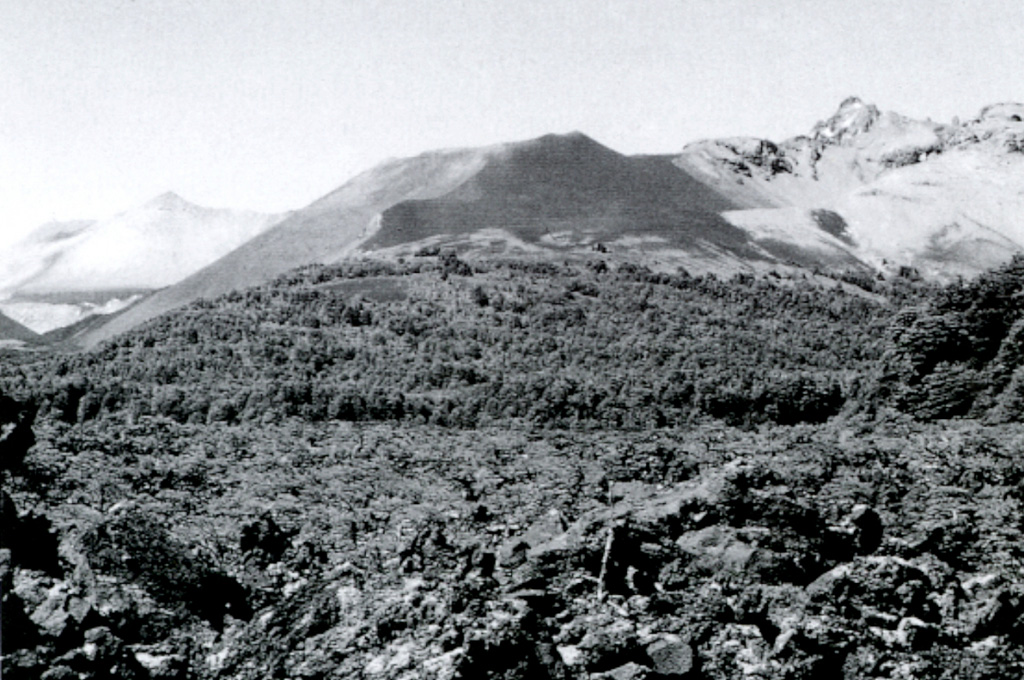 The blocky, partially forested Escorial lava flow in the foreground originated from Achín-Niellu (also known as Achen Niyeu or Cerro Escorial) pyroclastic cone (center).  The Escorial lava flow traveled north into glacial Lago Epulafquen, forming a prominent lava delta.  Oral accounts of local residents stated that the flow was witnessed by their grandparents, who described the eruption of smoke, ash, and lava that changed the shoreline of the lake. Photo by Moshe Inbar, 1995 (University of Haifa).