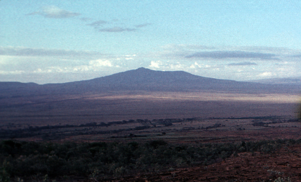 Longonot as seen from the flanks of Suswa volcano (SSW of Longonot) in the Eastern Rift Valley of Kenya. The modern cone was constructed within a broad 8 x 12 km caldera and itself contains a smaller 1.8-km-wide summit crater that gives the summit a flat profile. Post-caldera lavas are found on the caldera floor and on the flanks. Masai tradition records a lava flow on the N flank during the 19th century. Photo by Tom Jorstad, 1990 (Smithsonian Institution).