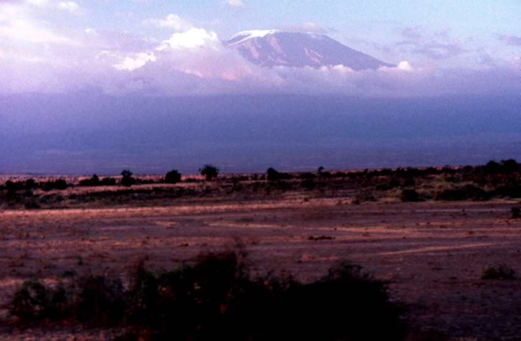 Massive Kilimanjaro, Africa's highest mountain, rises to the S above the Amboseli Game Preserve in Kenya. The 2.4 x 3.6 km caldera gives the ice-covered summit of Kibo an elongated, broad profile. Numerous smaller cones occupy a rift zone to the NW and SE of Kibo. Most of Kilimanjaro was constructed during the Pleistocene, but a group of nested summit craters are of apparent Holocene age. Photo by Tom Jorstad, 1990 (Smithsonian Institution).