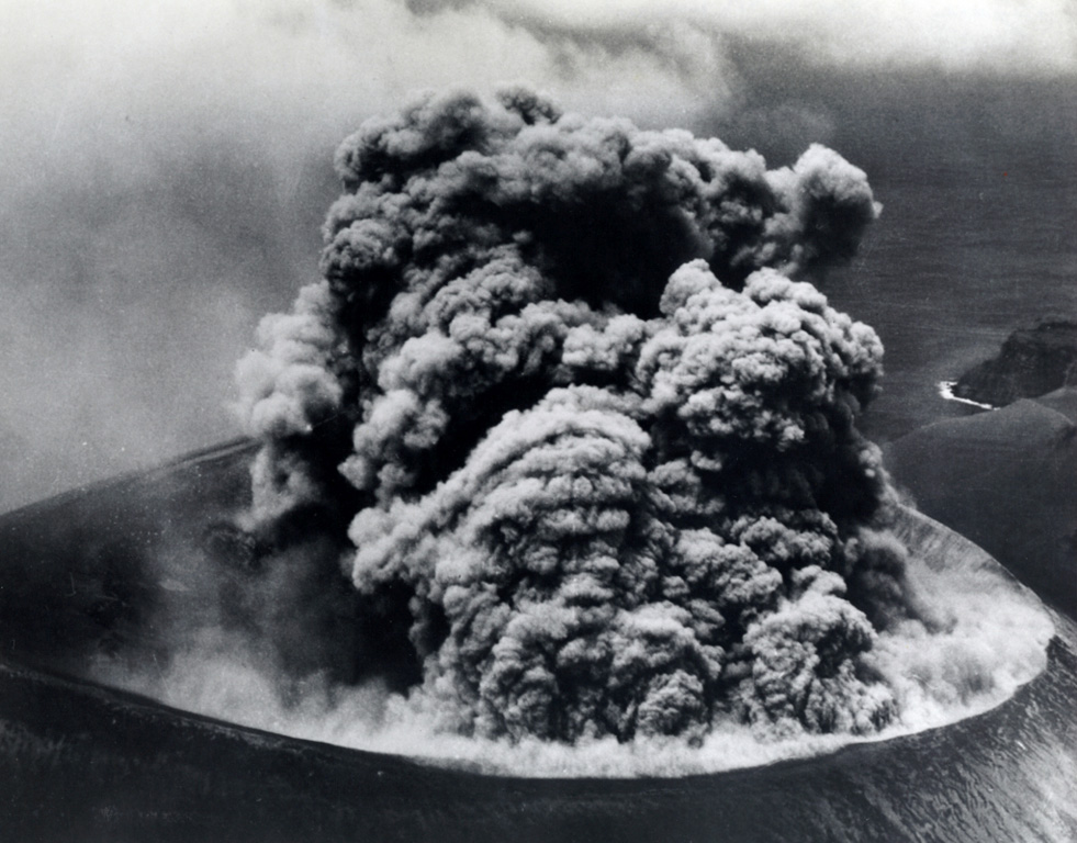 A Vulcanian ash plume rises from the Bárcena crater on 9 September 1952, more than a month after the start of the eruption. The roughly 300-m-wide crater is seen here from the east. Explosions producing eruption columns that rose to about 600 m above sea level were observed at 20-minute intervals, along with occasional small pyroclastic surges that swept down the flanks of the cone and sometimes reached the coast. The roar of the eruption was heard above the noise of the plane's engine. Photo by U.S. Navy, 1952 (courtesy of Sherman Neuschel, U.S. Geological Survey).