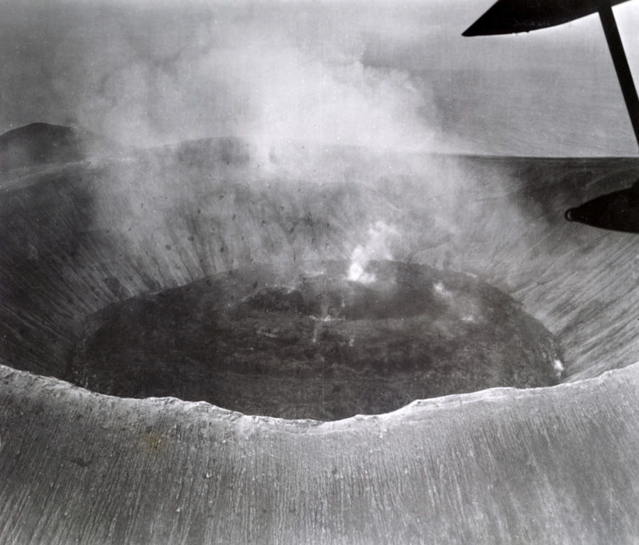 An overflight on 15 November 1952 shows the Bárcena crater half-filled with viscous lava. Sporadic small explosions were observed during the overflight, and continuous weak steam emission took place from the center of the dome. Montículo Cinerítico in the background and to the left is an eroded cone at the southern tip of the island that formed before the 1952 eruption. Photo by U.S. Navy, 1952 (courtesy of Sherman Neuschel, U.S. Geological Survey).