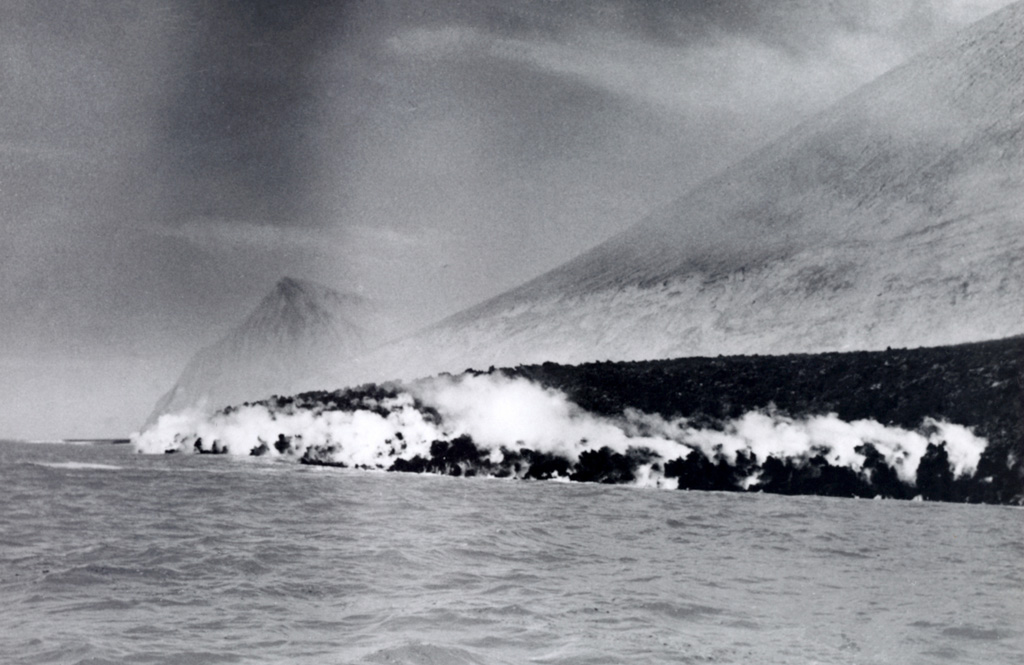 Entry of the Delta Lávico lava flow into the sea produces steam along the flow margins. The flow originated from a vent low on the Volcán Bárcena 1952-53 tuff cone. Punta Sur, the southernmost tip of the island, is in the left background and is a Montículo Cinerítico tuff cone that formed prior to the 1952 eruption and was formerly the highest point on the island. Photo by U.S. Navy, 1952 (courtesy of Sherman Neuschel, U.S. Geological Survey).