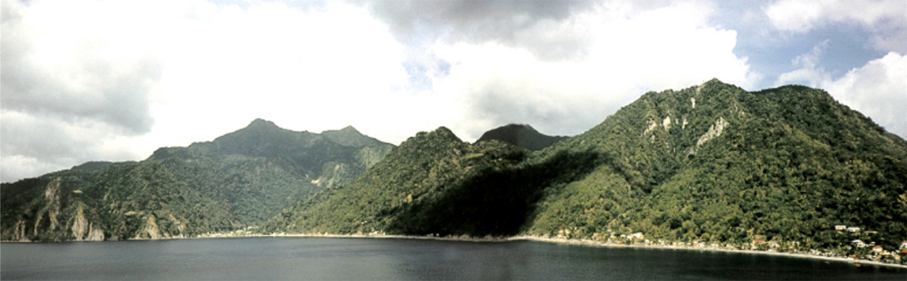 The 4-km-wide caldera of the Morne Plat Pays volcanic complex is widely breached to the sea of the west in this view from Scotts Head lava dome.  It formed about 39,000 years ago following a major plinian explosive eruption and flank collapse that truncated Morne Plat Pays stratovolcano, the peak on the left-center horizon.  The northern caldera margin lies immediately north of the post-caldera Socrière lava dome at the far left and near Soufrière village at the far right.  Post-caldera lava domes form the center-to-right horizon. Photo by Jan Lindsay, 2000 (Seismic Research Unit, University of West Indies).