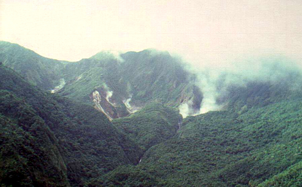 Fumarolic clouds mark the Valley of Desolation and Boiling Lake thermal areas, NE of Morne Watt (Watt Mountain) volcano in SE Dominica.  The Valley of Desolation and the Boiling Lake are major tourist attractions within the national park east of Roseau.  A major eruption from Morne Watt produced pyroclastic flows about 930 years ago.  The only historical eruptions on the island of Dominica were a moderately large phreatic explosion at the Valley of Desolation thermal area in 1880 and a smaller phreatic explosion in July 1997.   Photo by Paul Jackson, 1998 (Seismic Research Unit, University of West Indies).