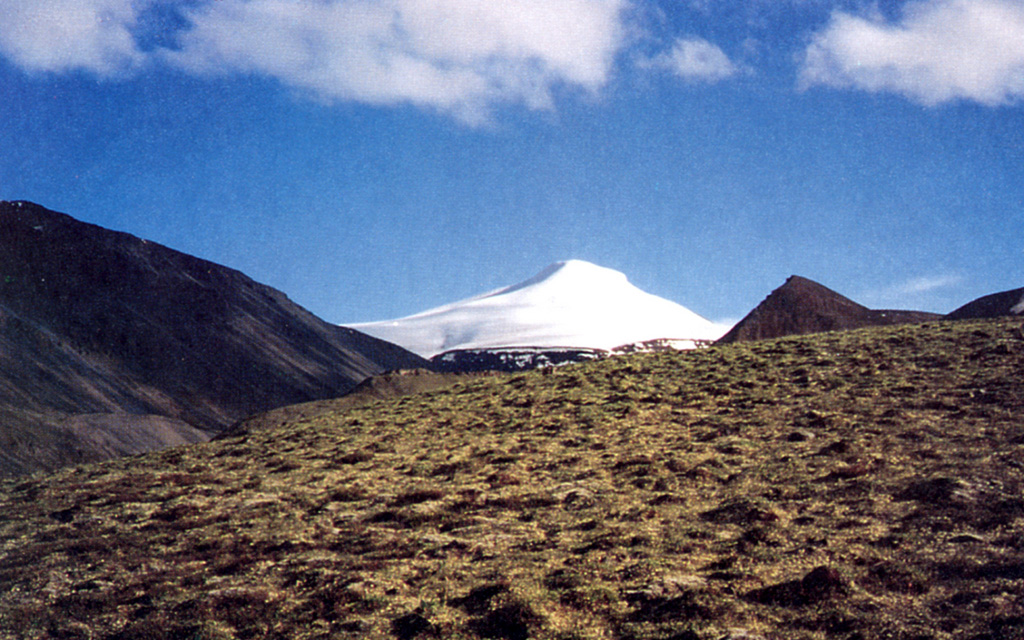 Snow-capped Mount Gordon is viewed here from the north.  The composite cinder-lava cone is 5 km in diameter and 625 m high.  A lava flow (out of view to the right) traveled from the base of the cone to the NW; tephra deposits from Mount Gordon are exposed primarily to the SW.  Mount Gordon is the most prominent of a group of Pleistocene and Holocene cinder cones in the northern Wrangell Mountains between Mount Drum and the Nabesna Glacier river system.   Photo by Donald Richter, 1994 (U.S. Geological Survey, published in Richter et al., 1995).