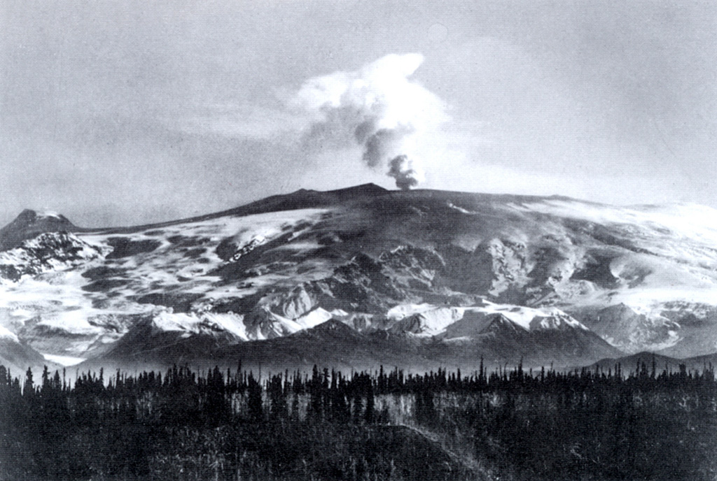 During a 1902 expedition in the Mount Wrangell area the U. S. Geological Survey scientist W.C. Mendenhall observed plumes and ash-covered snow. This photograph showing an ash plume rising above the summit crater was probably taken during the summer of 1902. Ash darkens the snow over a wide area of the southern flanks. The small cone on the far-left horizon is Mount Zanetti. Photo by W.C. Mendenhall, 1902 (U. S. Geological Survey).