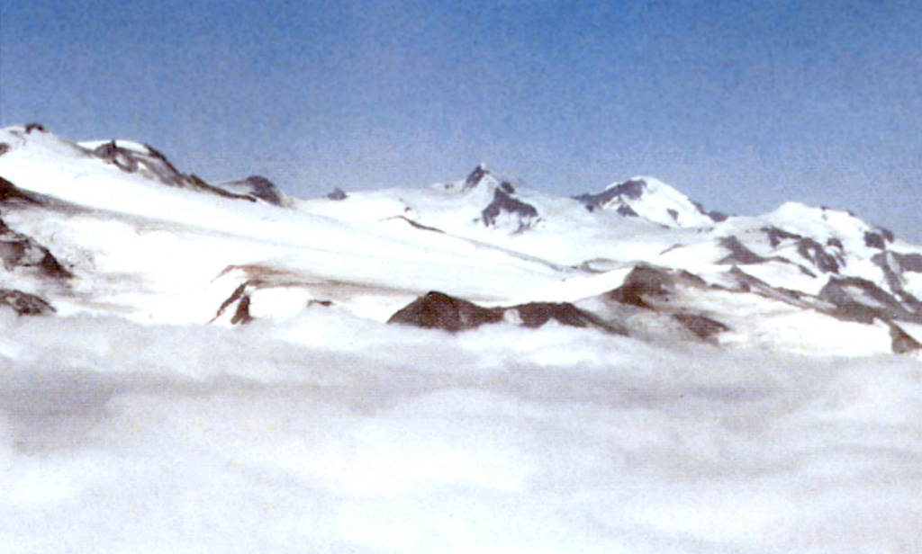 Mount Denison lies in a poorly known section of Katmai National Park that contains one or more mostly ice-covered vents. The slopes of Mount Denison are seen on the right half of the photo, between the pointed summit in the center and the flatter peak to the far right, between which a glacier descends towards the middle of the image. The rounded peak on the horizon beyond the slopes of Denison is Mount Steller, and the summit ridge of Snowy volcano forms the far-left skyline in this long-distance NE-looking view. Photo courtesy of Alaska Volcano Observatory, U.S. Geological Survey, 1997.
