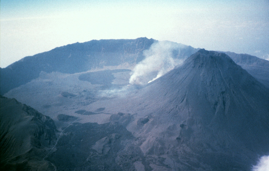 The 9-km-wide Cha caldera, open to the east, truncates the summit of Fogo stratovolcano. An ash plume (center) rises from an active vent on the western flank of the steep-sided Pico central cone (right). Pico is more than 1 km high and capped by an approximately 500-m-wide, 100-m-deep summit crater. Numerous historical eruptions have occurred from the summit of Pico and from its flanks in Cha caldera. Photo by Dick Moore, 1995 (U.S. Geological Survey).