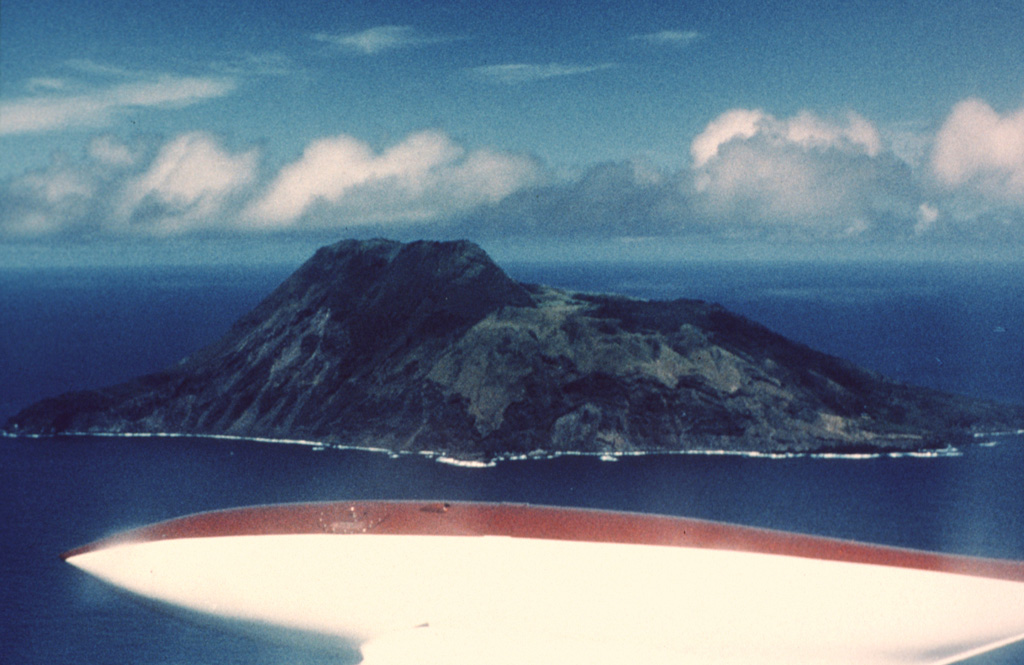 The 3-km-wide Sarigan volcano is seen here from the NE. The flat area to the right consists of a cone with a 750-m-wide summit crater that contains a small cone. The youngest eruptions produced two lava domes from vents on and near the S crater rim, forming the island's high point to the left. Holocene lava flows from the dome complex reached the coast to the left-center and formed the peninsula to the far left. Photo by Dick Moore, 1990 (U.S. Geological Survey).