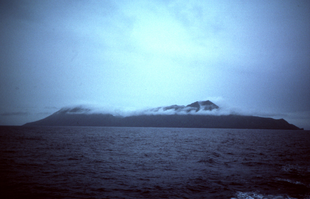 Two coalescing volcanoes form the 9-km-long island of Anatahan in the central Mariana Islands. The rim of a 2.5 x 5 km E-W-trending summit depression consisting of overlapping summit calderas forms the low point at the center of the island. Photo by Dick Moore, 1990 (U.S. Geological Survey).
