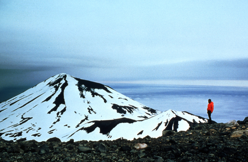 Korovin is seen here from the S, with the smaller Konia cone on its SE flank. Korovin is one of the most frequently active centers of the large complex at the NE tip of Atka Island, and contains two craters near the summit. The SE cone has a 1-km-wide crater, larger than the NW summit. Photo by Jim Myers, 1997 (University of Wyoming; courtesy of Alaska Volcano Observatory).