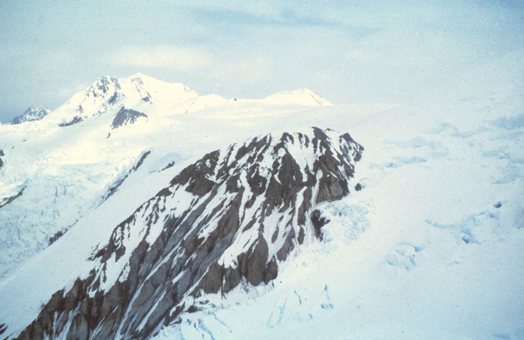 Hayes, located in a remote part of the Alaska Range, is almost totally covered by glacial ice and was not discovered until 1975. The volcano, named for the Hayes glacier, consists of remnants of a mostly snow-and-ice covered edifice that has been largely destroyed by catastrophic eruptions. The exposed rock in the foreground is South Dome. Hayes produced the most voluminous Holocene eruptions in the Cook Inlet area between about 3,800 and 3,400 years ago, and as recently as about 1,000 years ago. Photo courtesy of U.S. Geological Survey, Alaska Volcano Observatory.