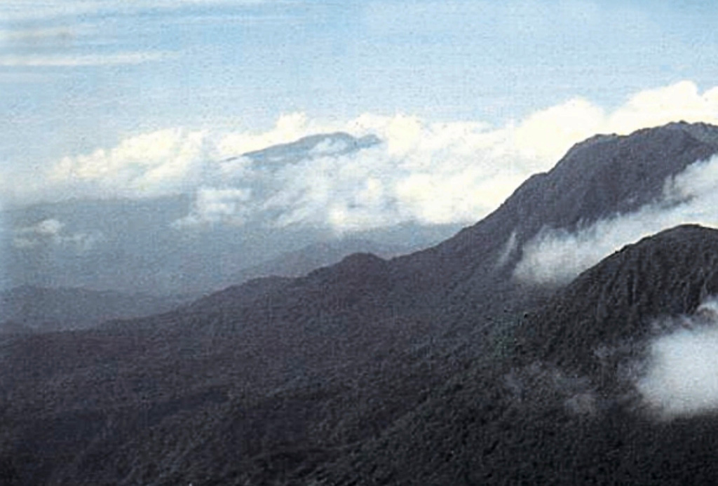 Cloud-draped Morne Diablotins (center) is the largest volcano on Dominica and one of the largest of the Lesser Antilles.  It is seen here from the south beyond Morne Trois Piton volcano at the far right.  Two coalescing lava domes form the summit of 1430-m-high Morne Diablotins, and precolumbian pyroclastic-flow aprons on the NW flank are relatively unmodified by erosion.  Historical eruptions are not known from Morne Diablotins.  However the volcano has a youthful appearance, and seismic swarms have occurred nearby in recent years.   Photo by Paul Jackson, 1998 (Seismic Research Unit, University of West Indies).