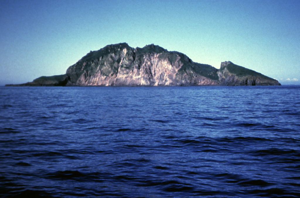 A steep, arcuate cliff drops nearly 300 m to the coast on the western side of Koniuji Island. This small, 1 x 1.5 km wide island, located between Atka Island and Kasatochi volcano, is the emergent top of a mostly-submarine volcano. A NE-trending fault is visible on the SE side of the island (right).  Photo by E. Bailey, 1982 (U.S. Fish and Wildlife Service).