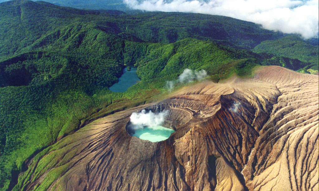 This aerial photo from the north overlooks the Rincón de la Vieja summit cone complex in NW Costa Rica. A gas plume rises from the acidic Cráter Activo lake, and erosional gullies have formed across the flanks. The darker Laguna Fria beyond the Cráter Activo is a non-volcanic lake formed between the vegetated Rincón de la Vieja crater (far-left) and the ridge extending to Santa María to the upper left of the photo.  Photo by Federico Chavarria Kopper, 1996.