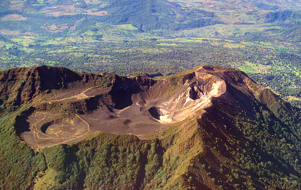 The Turrialba summit crater complex is seen here from the north, with the Central Valley of Costa Rica in the background. Three well-defined craters can be seen at the upper SW end of the broad summit area. Hydrothermally altered deposits can be seen at the central and SW summit craters (right), where geothermal activity continues.  Photo by Federico Chavarria Kopper, 1999.
