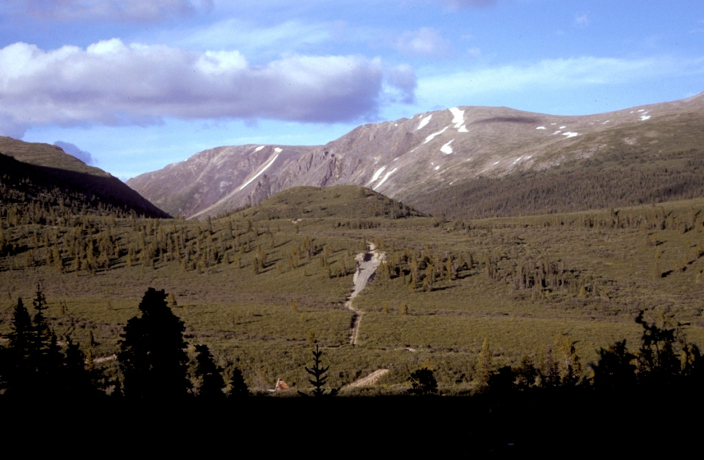 Cracker Creek cone (center), the small vegetated hill seen here from the west, is the youngest feature of the Atlin Volcanic Field on the Teslin Plateau in NW British Columbia. The small scoria cone lies at the head of Cracker Creek, immediately east of Ruby Mountain volcano, and may have been the source of a large lava flow that partly filled Ruby Creek. The lower west side of the cone appears to be partly covered by glacial till, suggesting that the cone is older than the most recent glacial advances down Ruby Creek. Photo by Ben Edwards, 2000 (Dickinson College, Pennsylvania).