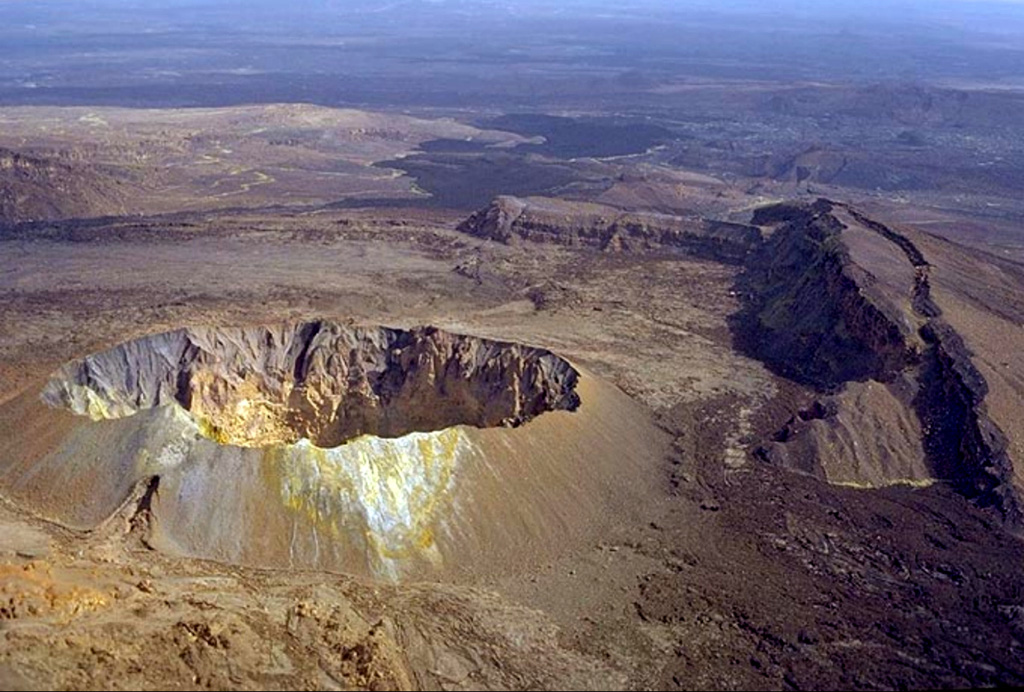 A symmetrical scoria cone with a 200-m-wide crater lies in the center of a graben that cuts the summit of Hayli Gubbi volcano, the southernmost in the Erta Ale Range. The cliffs at the right form the W side of the graben. Dark lava flows seen at the top center were erupted from the axial portion of a fissure system that extends for more than 10 km to the S. The lava flows have reached the floor of the Giulietti plain S of the Erta Ale Range. A steam plume was observed from the crater in February 2002. Copyrighted photo by Marco Fulle, 2002 (Stromboli On-Line, http://stromboli.net).