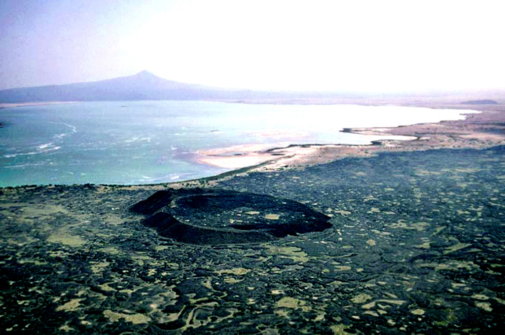 On the horizon, Afderà volcano is located SW of Lake Afrera (Lake Giulietti). This isolated rhyolitic stratovolcano is located at the intersection of three fault systems between the Erta Ale, Tat Ali, and Alayta ranges. The low lakeshore tuff ring in the foreground is surrounded by lava flows erupted from vents SE of Hayli Gubbi volcano. Photo by Jürg Alean, 2002 (Kantonsschule Zürcher Unterland, Bülach, Switzerland).