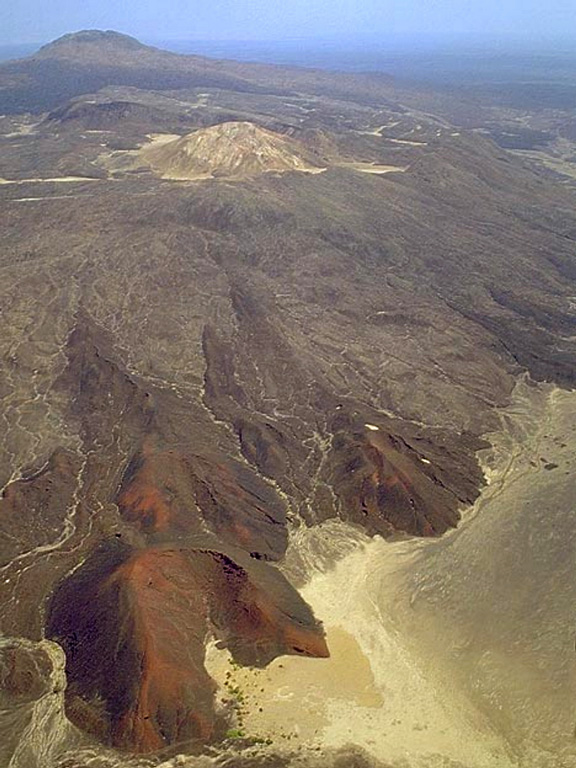 The summit of Borale Ale (upper left) consists of a silicic stratovolcano that is the largest of the Erte Ale Range. Spatter cones aligned along regional fissures can be seen in the foreground and an altered lava dome forms the light-colored cone above the fissures. Strong fumarolic activity occurs within a 300-m-wide crater on the 668-m-high summit of the volcano. Regional faulting has resulted in recent basaltic lava flows from a NNW-trending fissure that cuts the stratovolcano. Copyrighted photo by Marco Fulle, 2002 (Stromboli On-Line, http://stromboli.net).