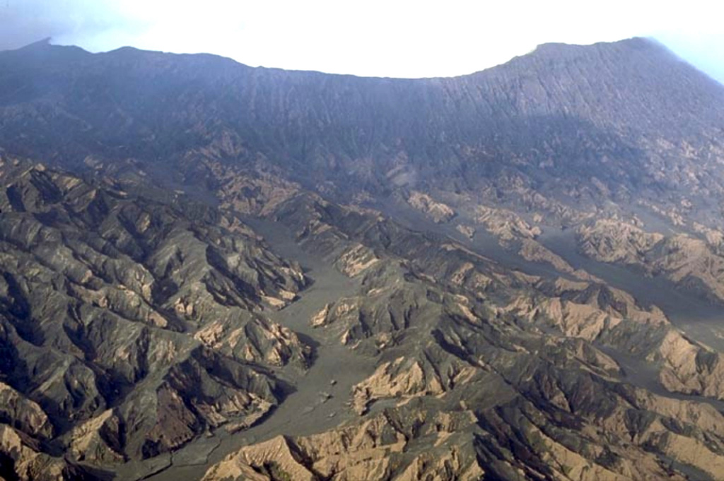 Erosional gullies in fresh tephra deposits across the northern slopes of Benbow, one of the tuff cones in the Ambrym summit caldera. The 12-km-wide caldera formed during a major Plinian eruption with dacitic pyroclastic flows about 1,900 years ago. Post-caldera eruptions, primarily from the Marum and Benbow cones, have partially filled the caldera floor and produced lava flows that ponded on the caldera floor or overflowed through gaps in the caldera rim. Copyrighted photo by Marco Fulle, 2000 (Stromboli On-Line, http://stromboli.net).